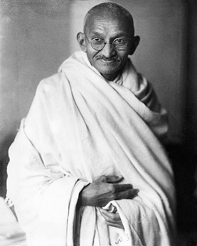 Mahatma Gandhi, embodying the philosophy of the spinning wheel and self-reliance, who led the Indian independence movement. He stands with a dignified expression, wearing white khadi attire.