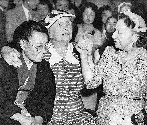 Helen Keller sentada junto a una mujer japonesa en kimono. Ambas están sonriendo.