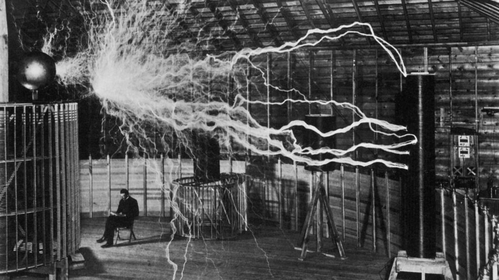 Nikola Tesla assis à côté de son transmetteur amplificateur, démontrant l'électricité sans fil dans son laboratoire, vers 1899.